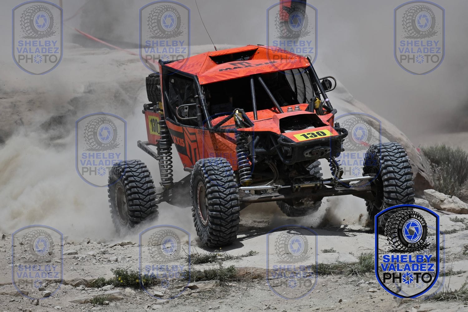 Orange Ultra4 car number 150 powering across the rocks in a cloud of dust