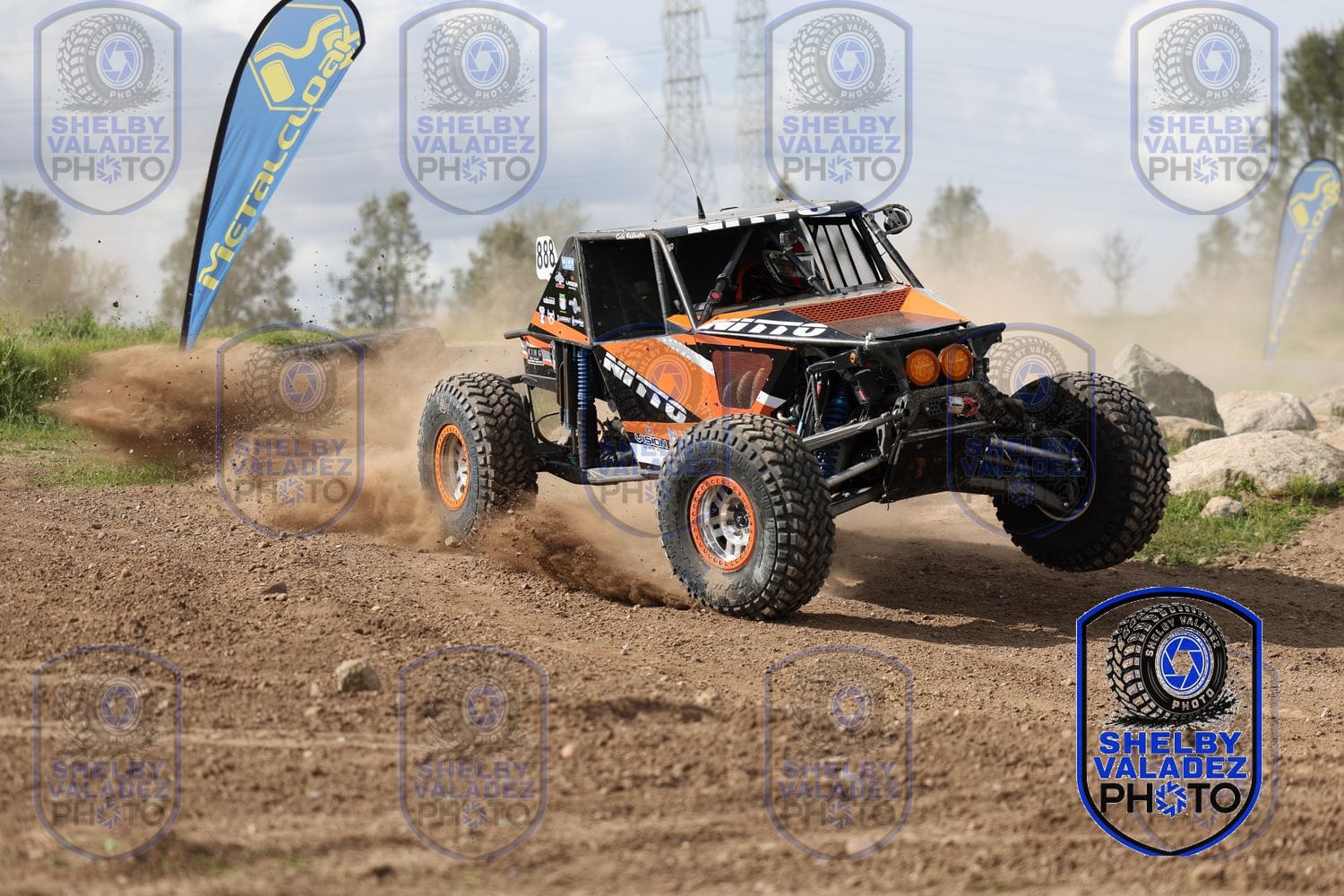 Orange Ultra4 car sliding through a dirt corner past a banner